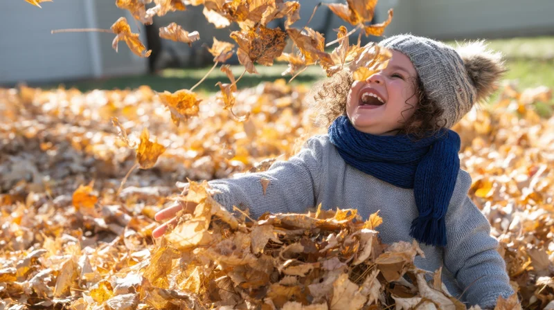Toddler laughing while playing in a pile of autumn leaves outdoors