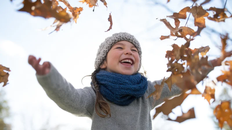 Laughing girl in autumn leaves outdoors wearing cozy knit hat and scarf