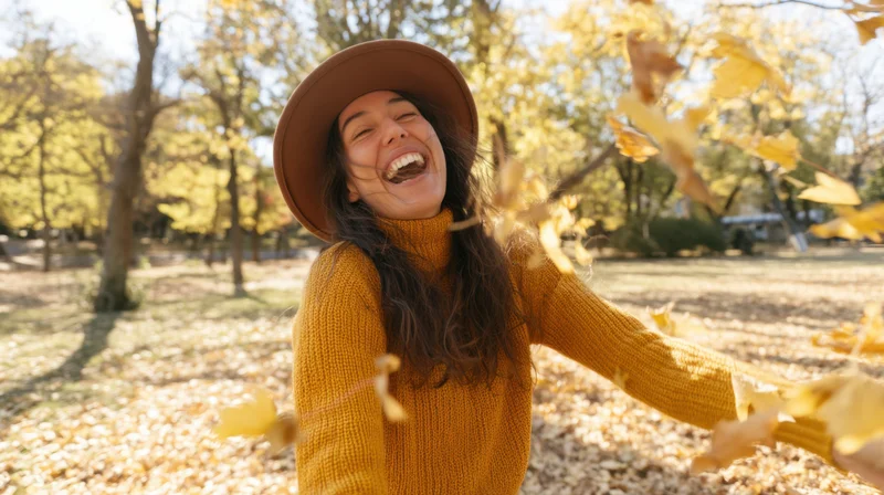 Young woman laughing and throwing leaves in a sunlit autumn park