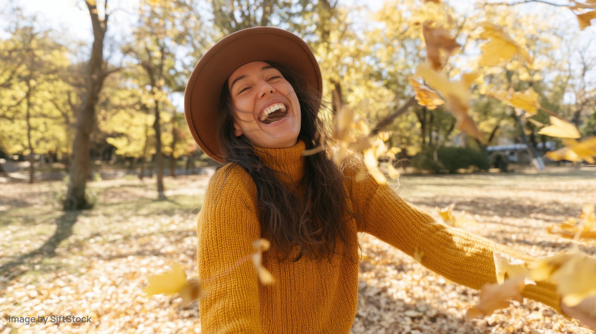 Young woman laughing and throwing leaves in a sunlit autumn park