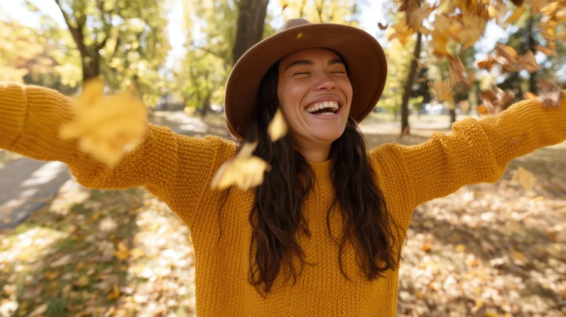 Young woman laughing with arms outstretched in a park covered in autumn leaves