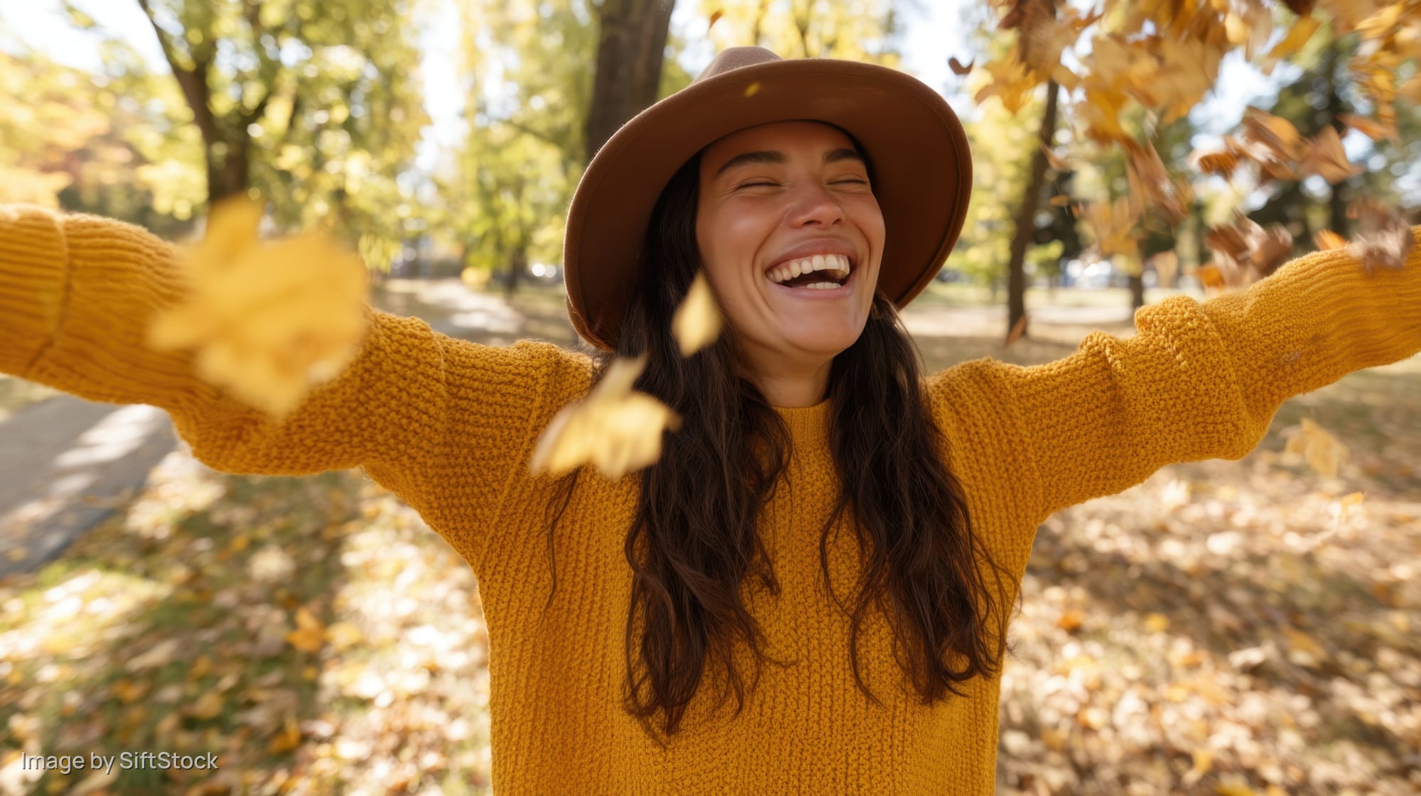 Young woman laughing with arms outstretched in a park covered in autumn leaves