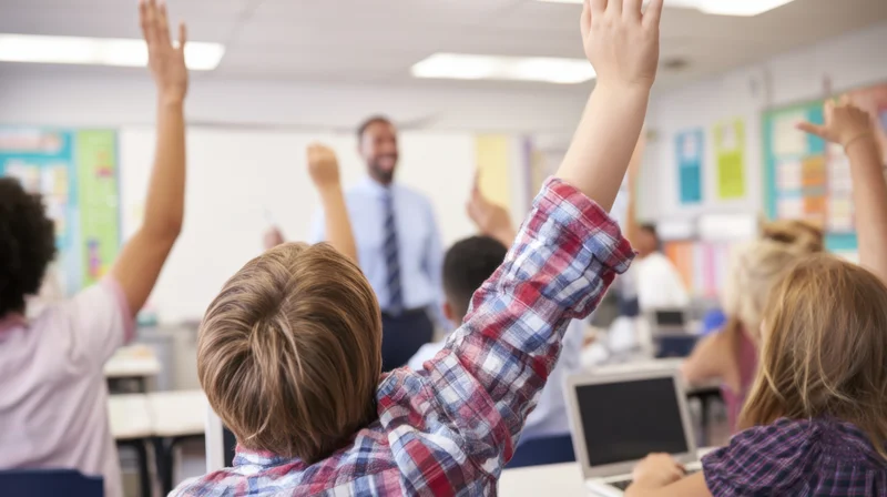 Students raising hands in a classroom with a teacher leading a lesson