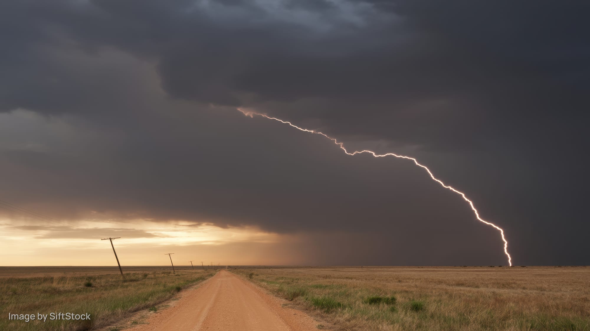 Lightning striking over a dirt road in an open field under storm clouds