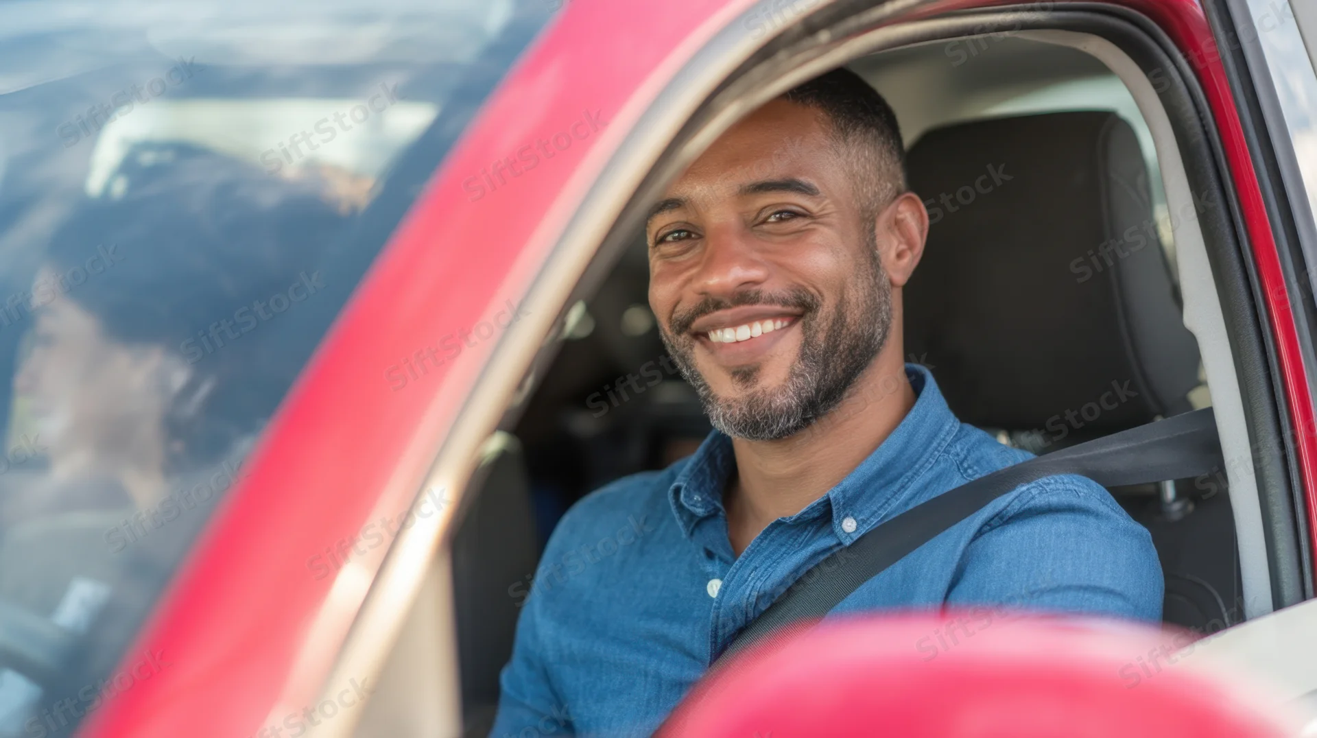 Smiling man in blue shirt driving a red car with seatbelt fastened