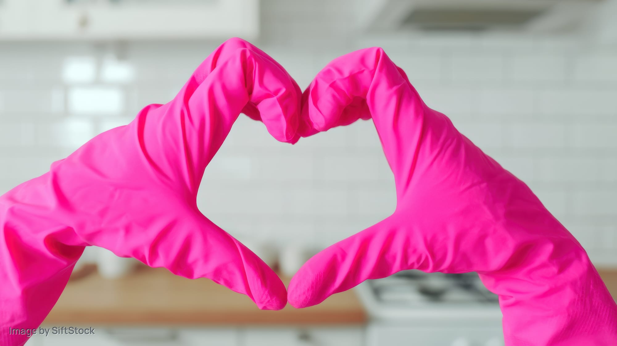 Hands in pink rubber gloves forming heart shape in kitchen