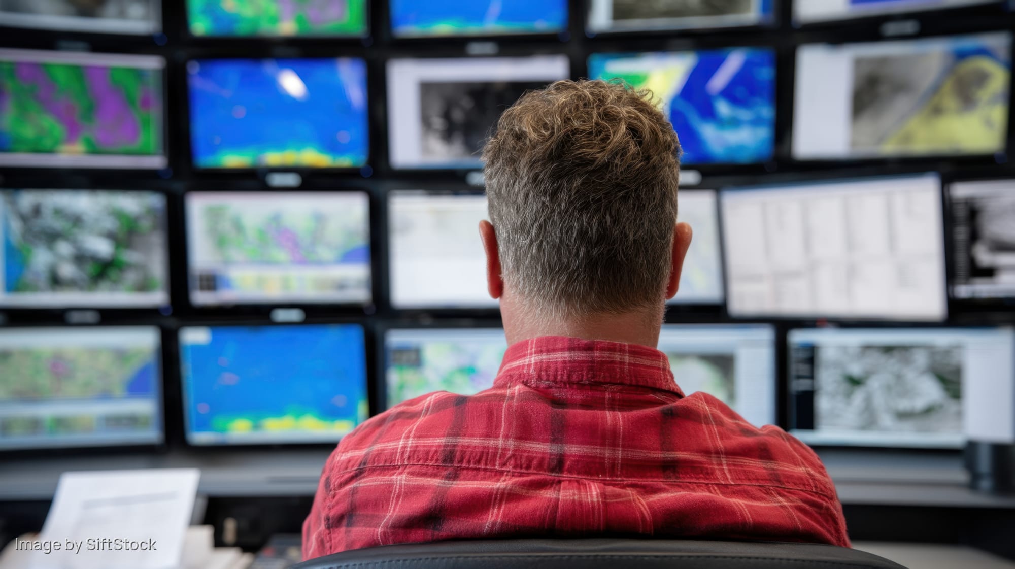Man in red plaid shirt monitoring multiple screens in a control room