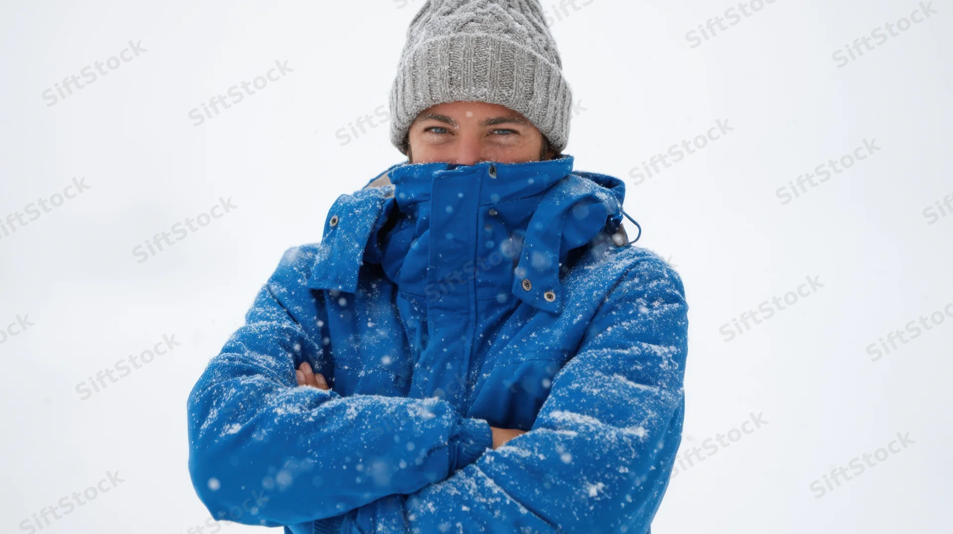 Woman in blue winter jacket with arms crossed, snow falling, outdoors