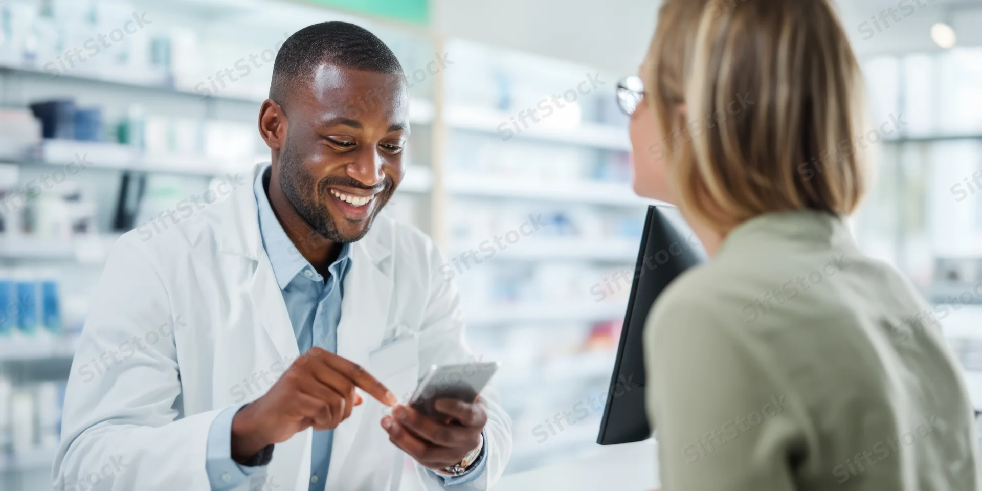 Pharmacist in white lab coat smiling while showing smartphone to patient at pharmacy counter