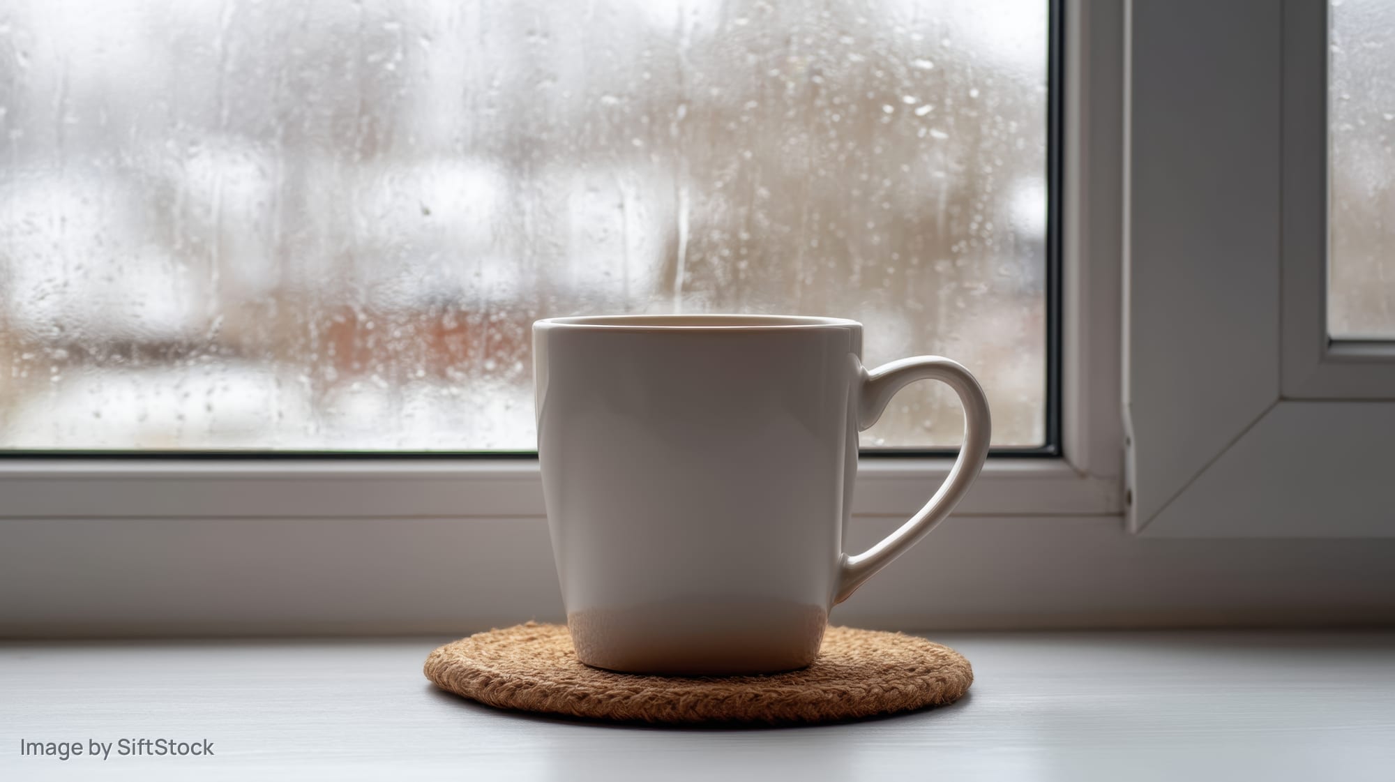 White ceramic mug on woven coaster by rain-streaked window sill
