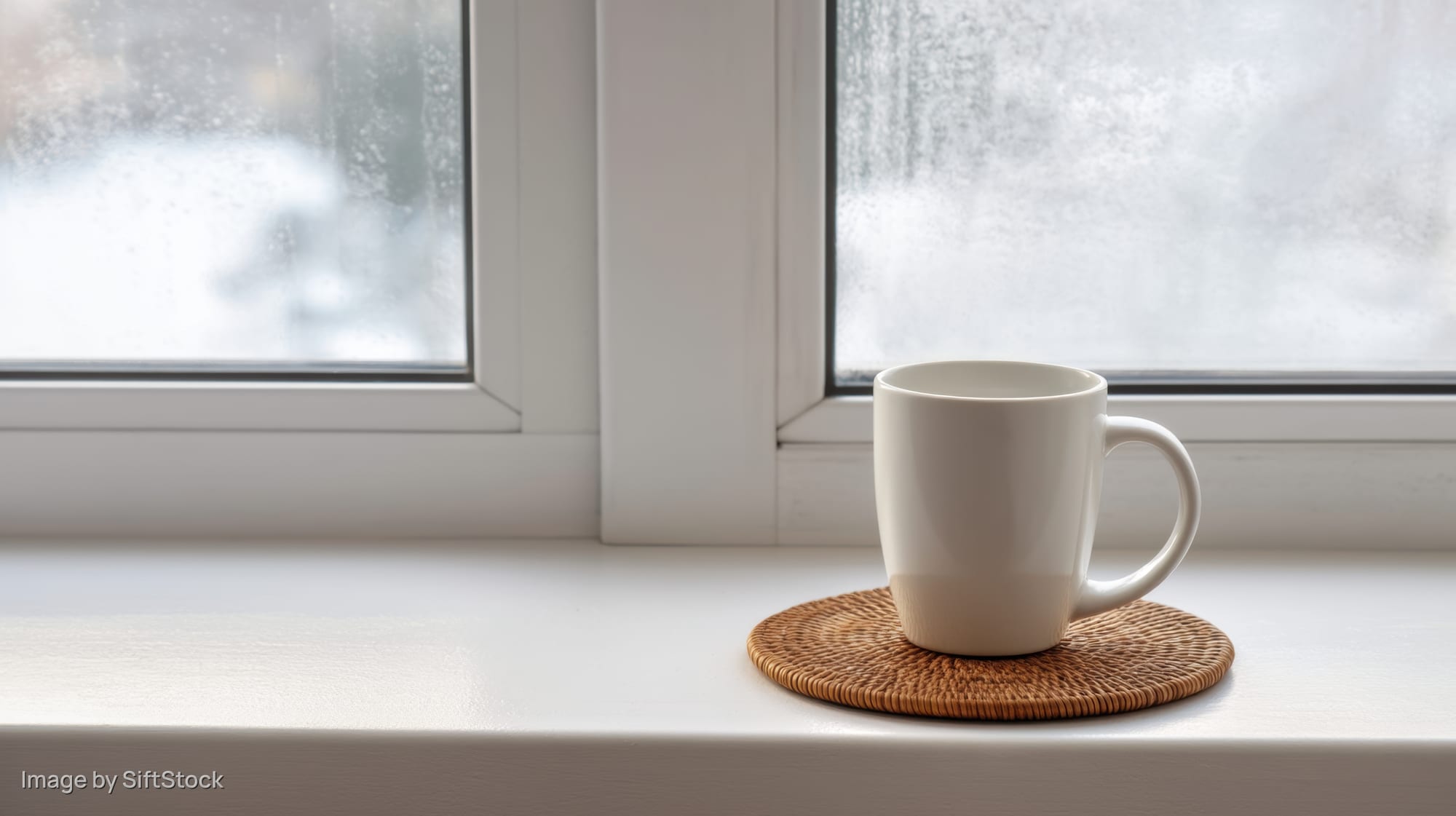 White ceramic mug on woven coaster on windowsill with snowy view outside