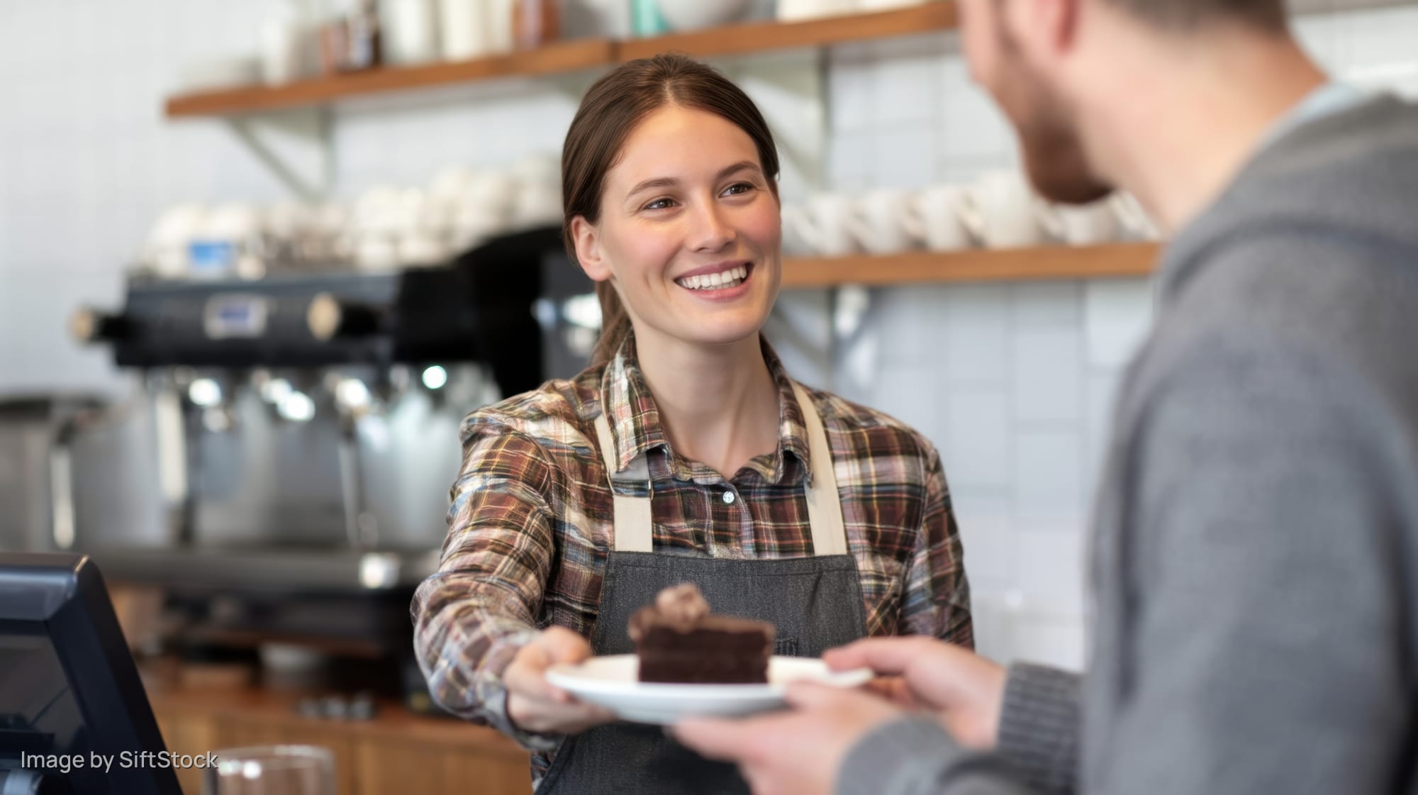Smiling barista handing chocolate cake on plate to customer at cafe counter