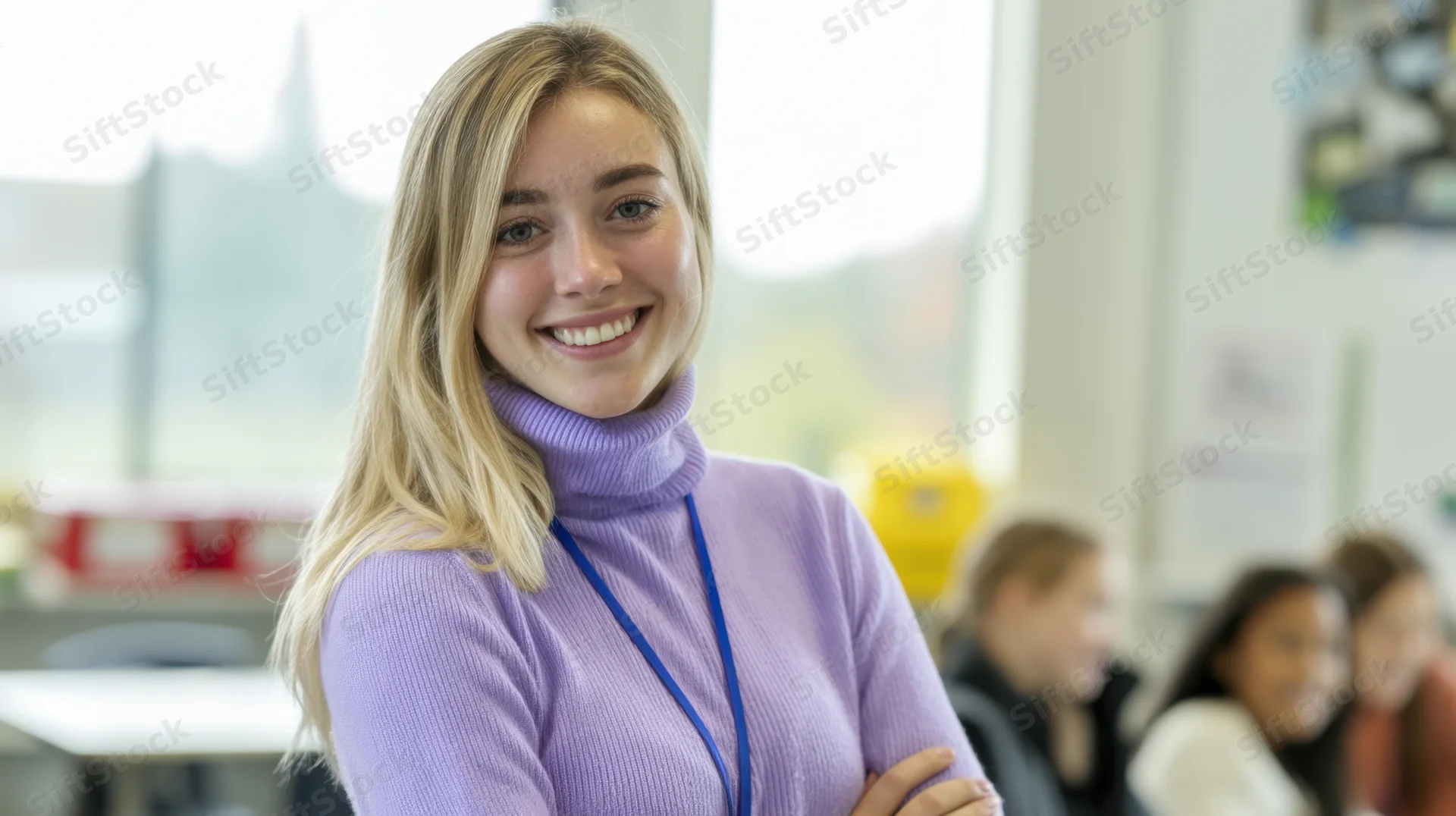 Smiling blonde woman in purple turtleneck standing in classroom with students in background