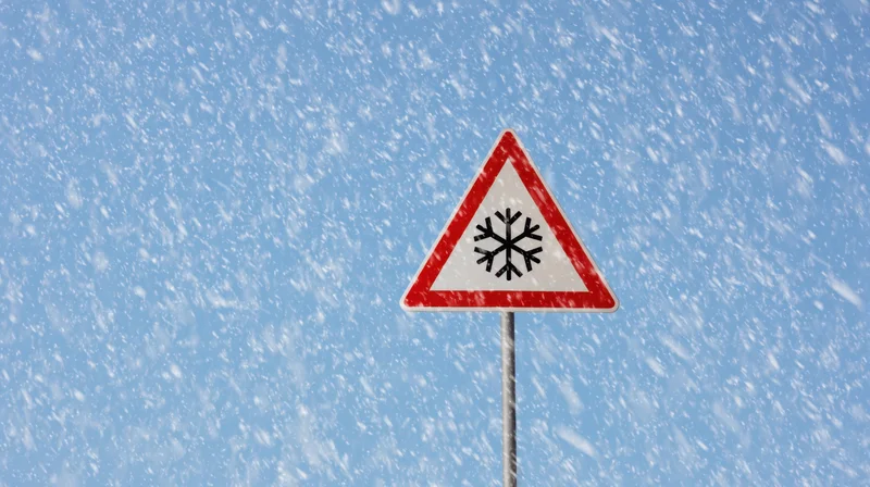 Triangular warning sign with snowflake symbol against blue sky during snowfall