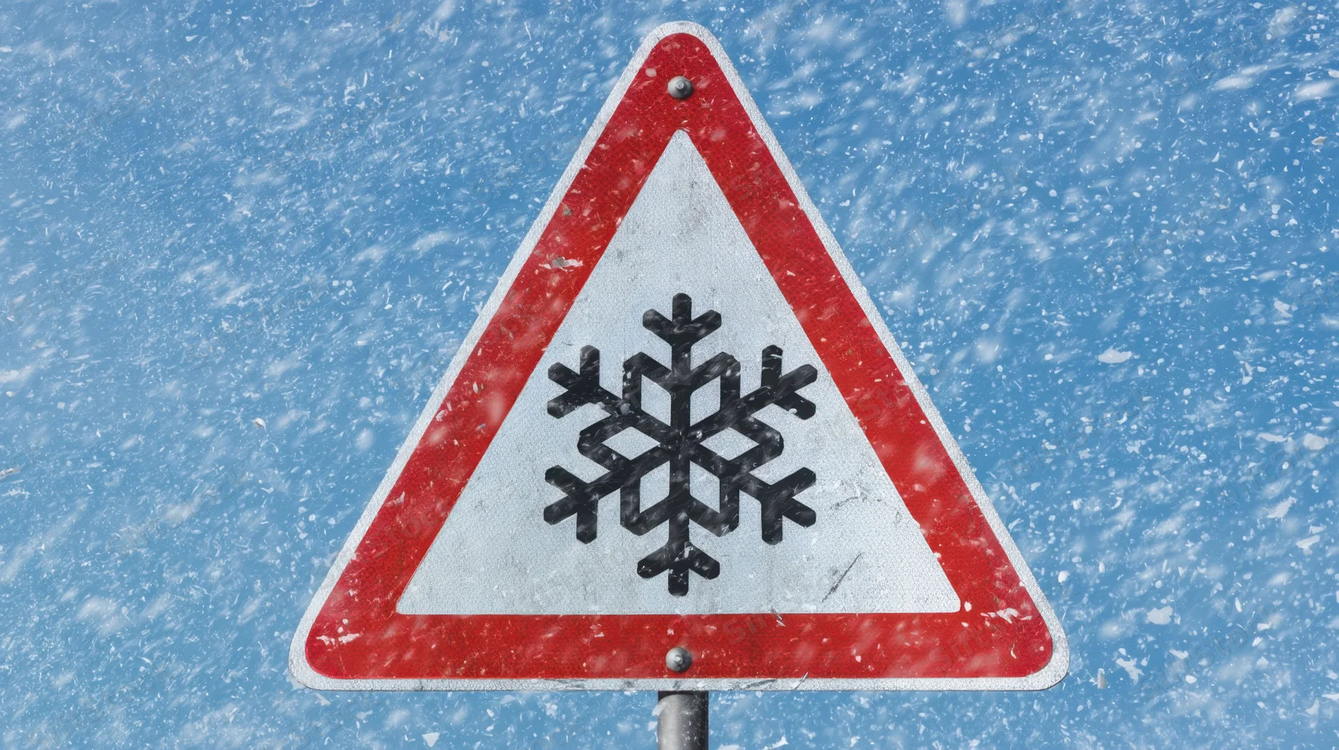 Triangular warning sign with snowflake symbol against blue sky during snowfall