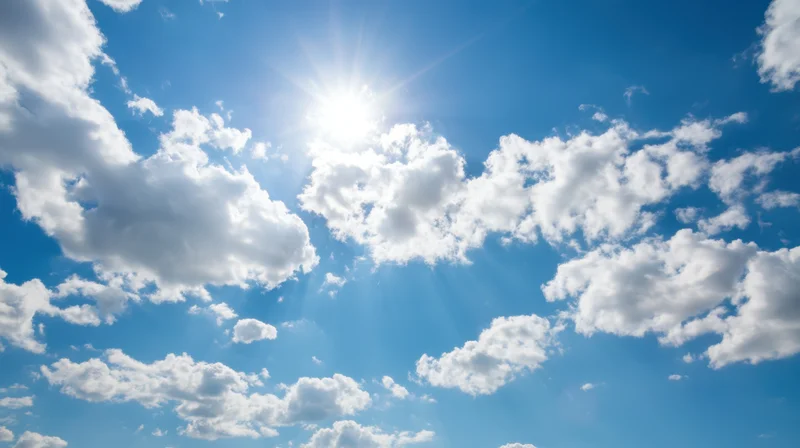 Bright sun shining through scattered white clouds in a vivid blue sky