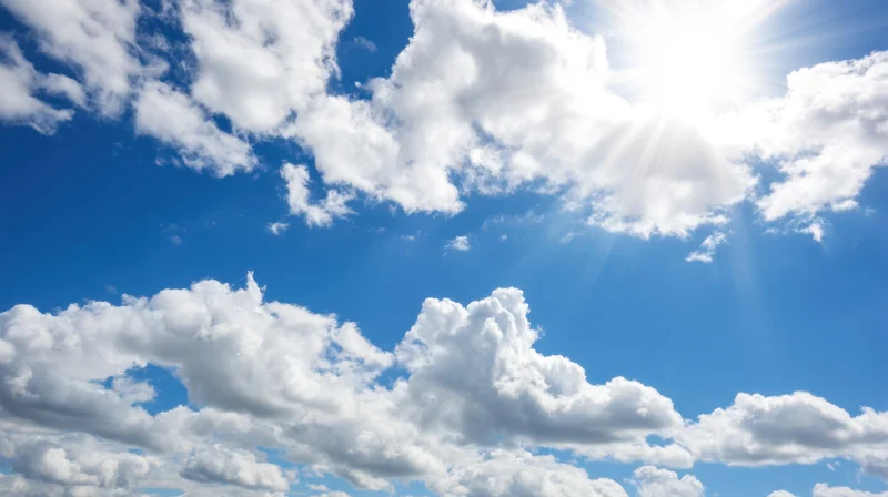 Bright blue sky with white clouds and sunbeams visible above the horizon