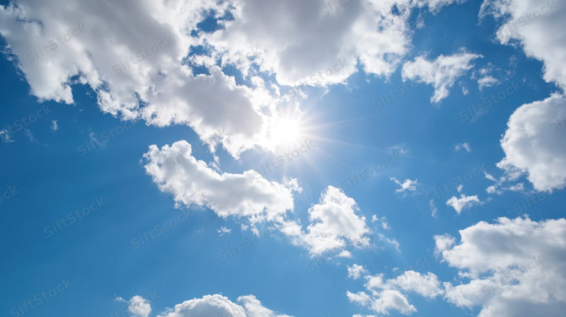 Bright sun shining through scattered white clouds in a vivid blue sky