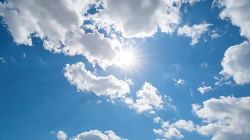 Bright sun shining through scattered white clouds in a vivid blue sky