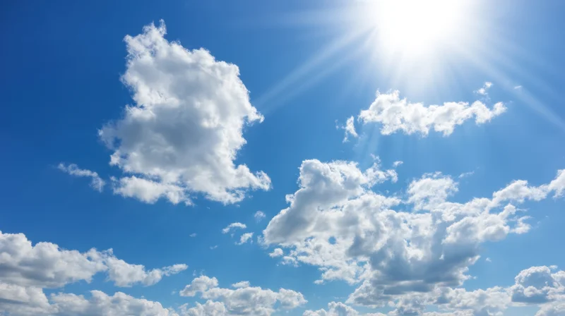Bright sun shining through white clouds in a vivid blue sky