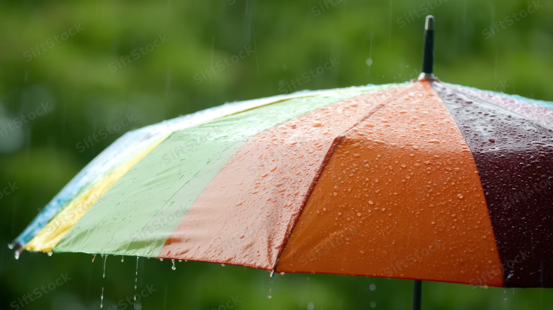 Rainbow umbrella open in rain with water droplets on colorful panels against green foliage background
