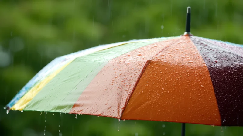 Rainbow umbrella open in rain with water droplets on colorful panels against green foliage background