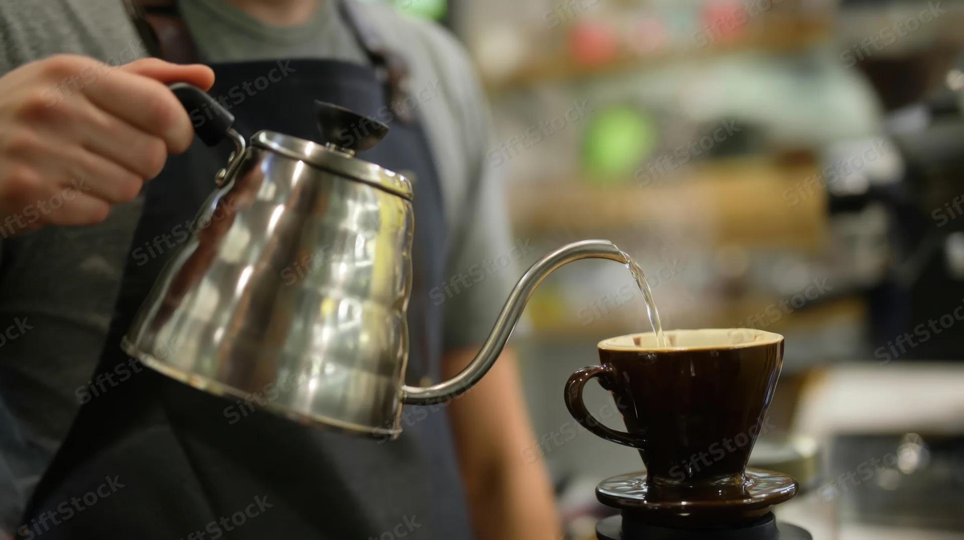 Barista pouring hot water from a gooseneck kettle into a ceramic coffee filter in a cafe