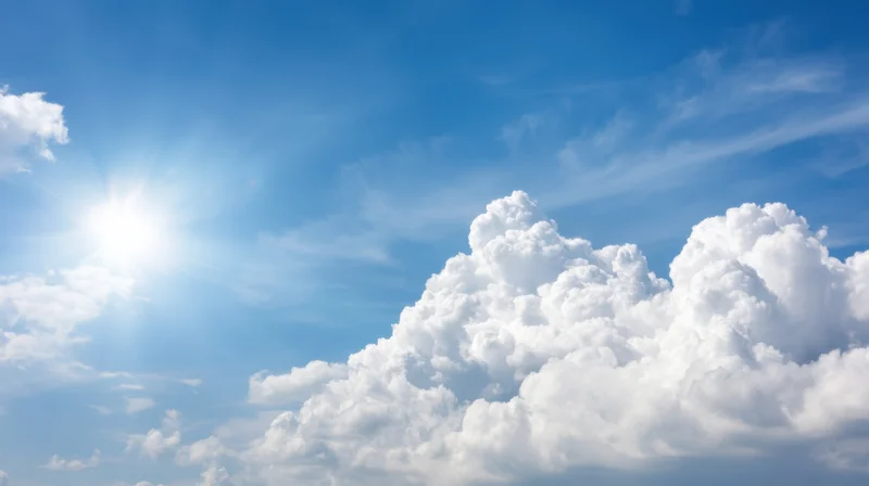 Bright sun shining in a clear blue sky with large white cumulus clouds