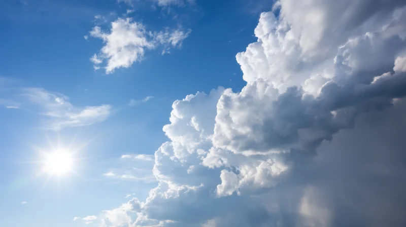 Bright sun shining in a blue sky with large white cumulus clouds