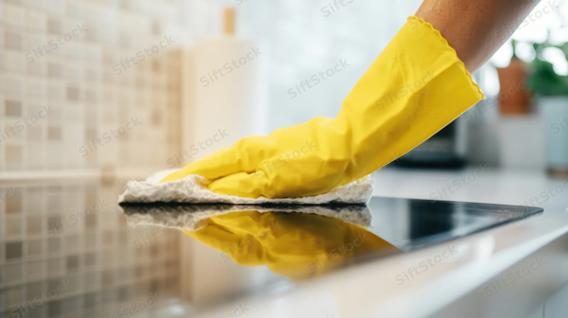 Hand in yellow rubber glove wiping kitchen countertop with sponge