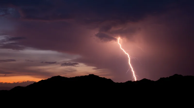 Lightning striking over mountain silhouette at sunset