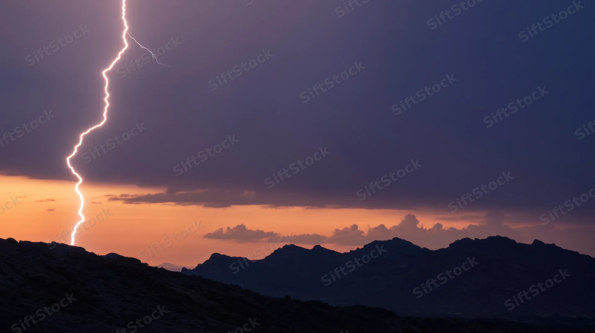 Lightning striking over mountain range at sunset