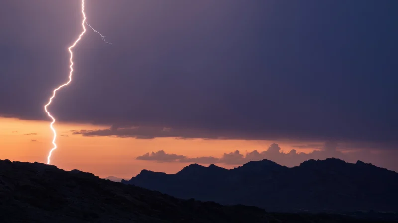 Lightning striking over mountain range at sunset