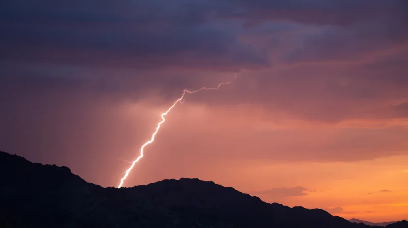 Lightning striking over mountain silhouette at sunset