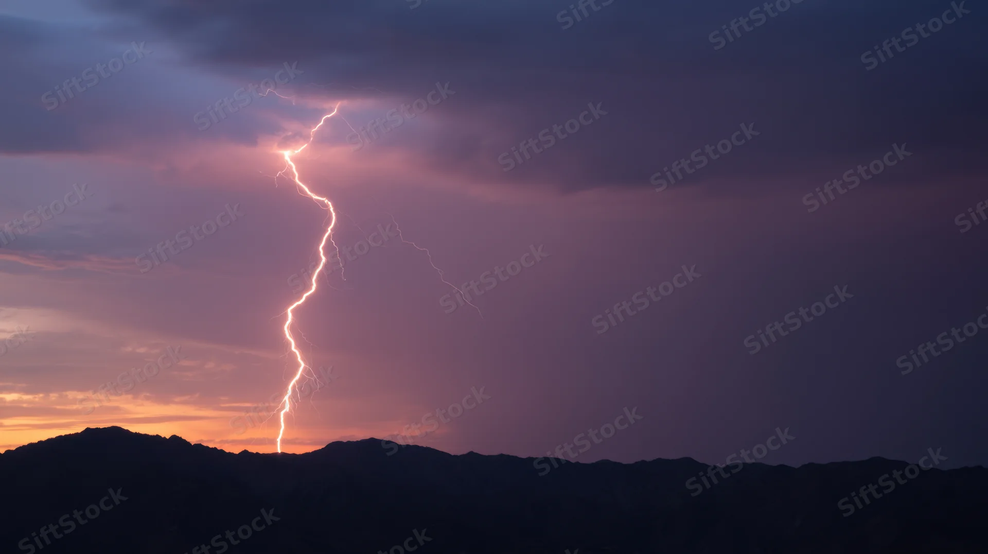 Lightning striking above mountain silhouette at sunset