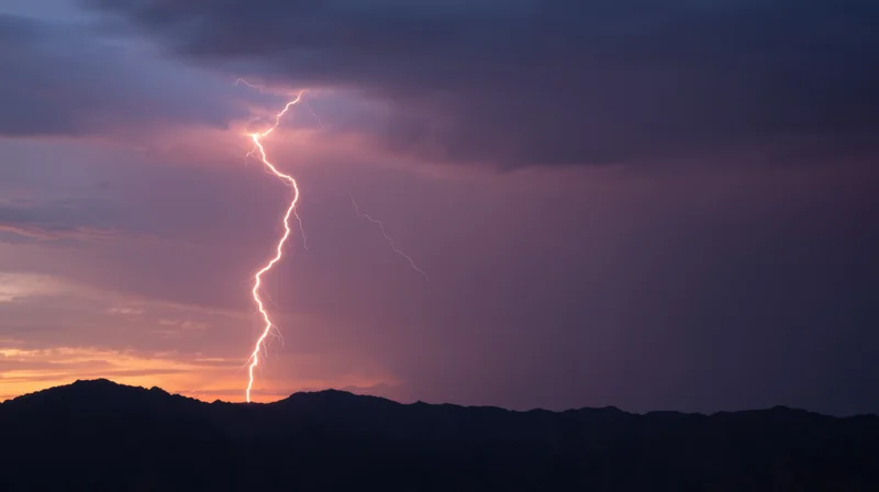 Lightning striking above mountain silhouette at sunset
