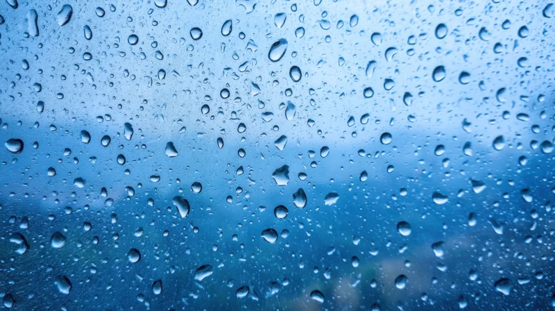 Raindrops on a glass surface with blue sky visible through the water droplets