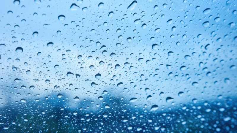 Raindrops on a glass window with blurred blue sky background