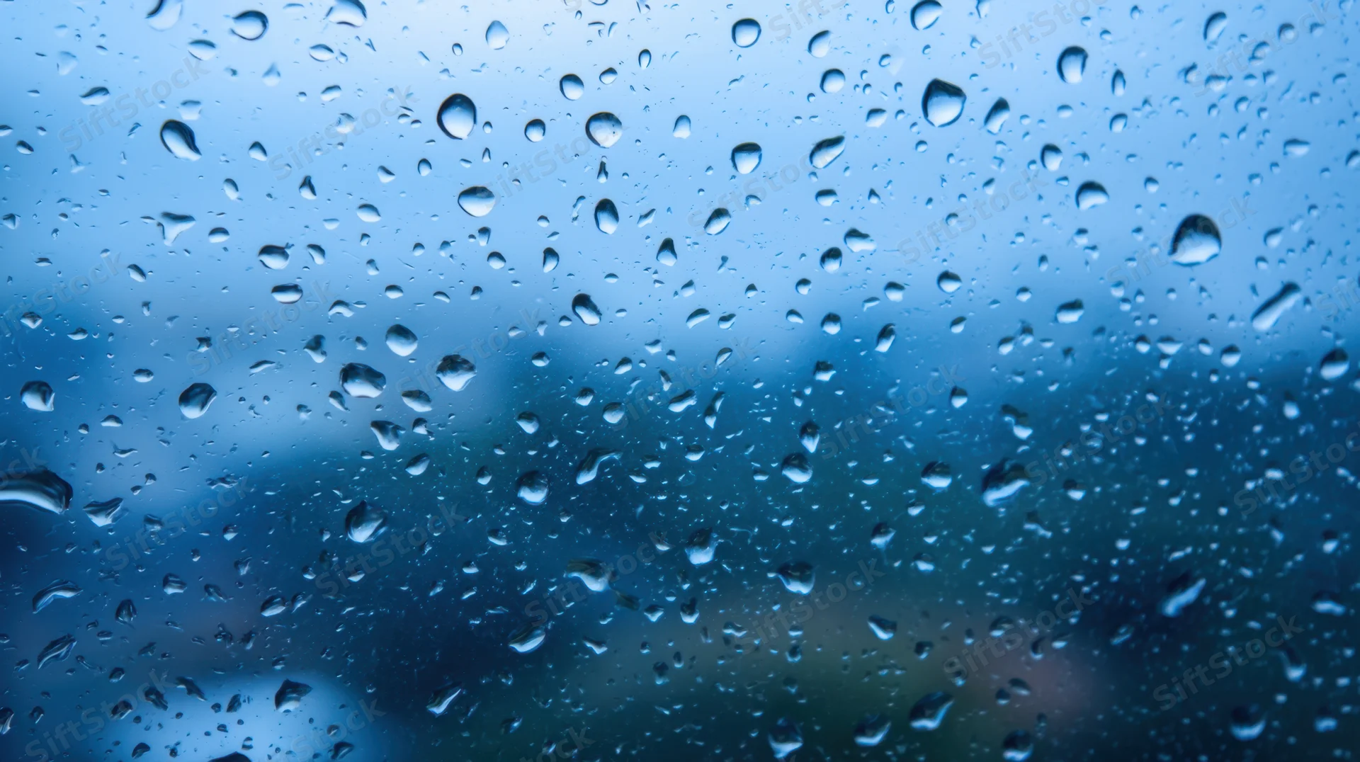 Raindrops on a glass window with blurred blue sky background