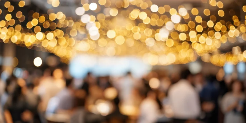 Blurred view of a crowded indoor reception with golden string lights overhead