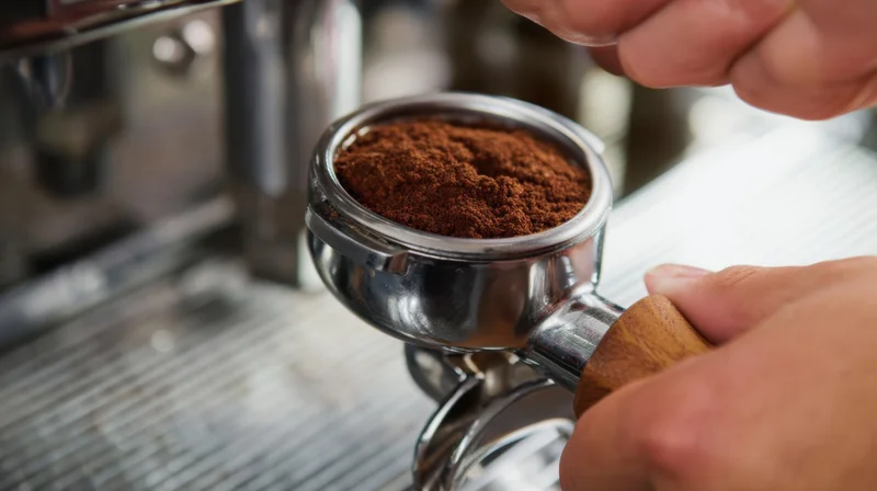 Barista tamping fresh coffee grounds in a portafilter at a cafe
