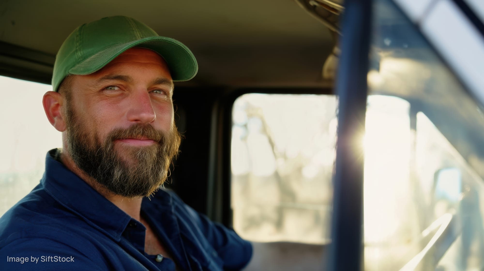Bearded man smiling inside truck cab during daytime