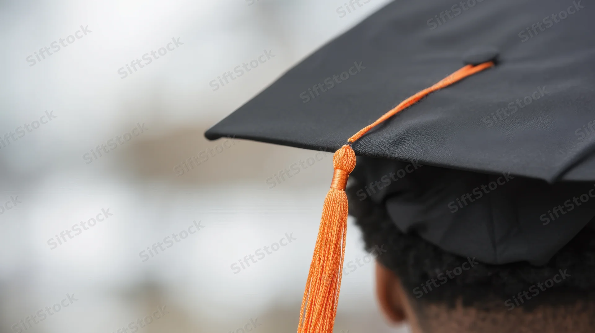 Closeup of a black graduation cap with orange tassel on a young man's head