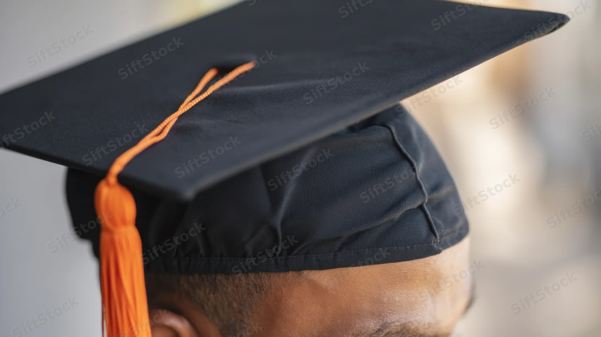 Closeup of a young africanamerican male wearing a black graduation cap with orange tassel in profile view