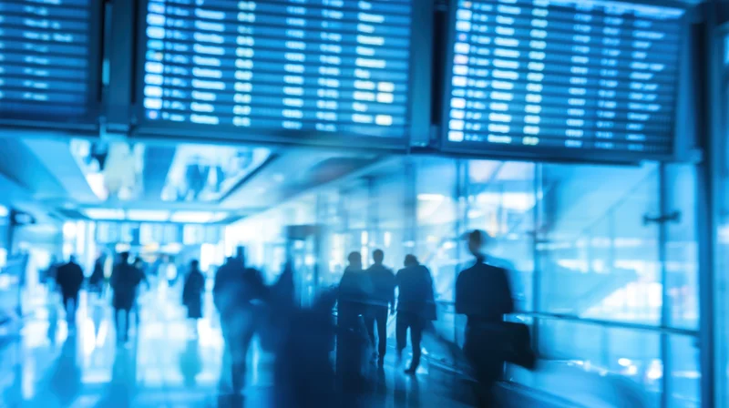 Silhouetted travelers moving through a blue-lit airport terminal with digital flight displays above