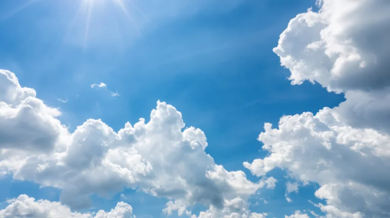 Bright blue sky with white cumulus clouds and sunbeams visible above