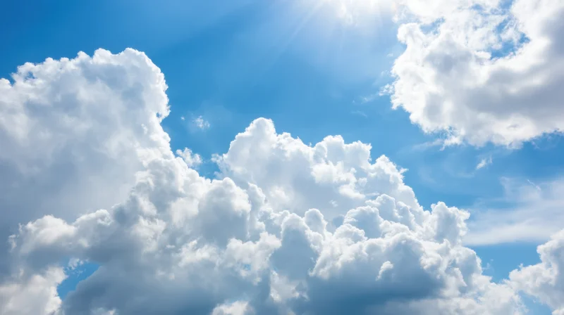 Bright blue sky filled with fluffy white cumulus clouds and sunbeams