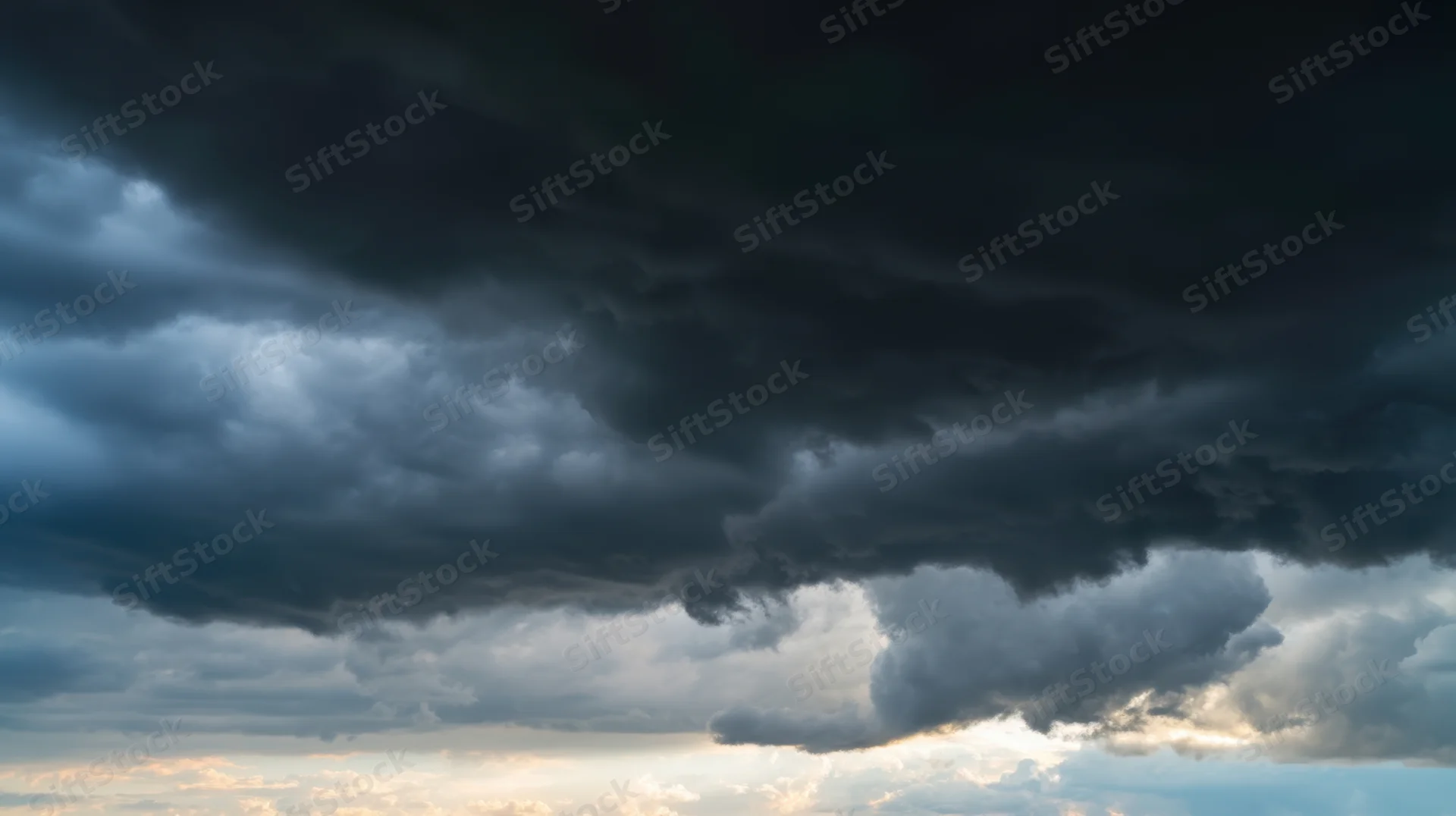 Dark storm clouds dominating the sky with sunlight breaking through at the horizon