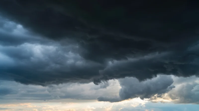 Dark storm clouds dominating the sky with sunlight breaking through at the horizon