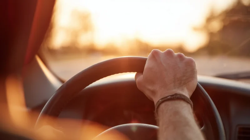 Hand gripping steering wheel inside car during sunset drive